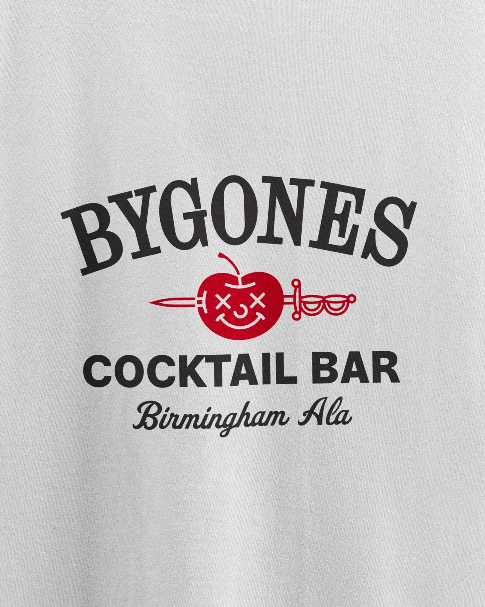 T-shirt featuring 'BYGONES COCKTAIL BAR Birmingham Ala' text with an apple pierced by a sword, set against a white background.