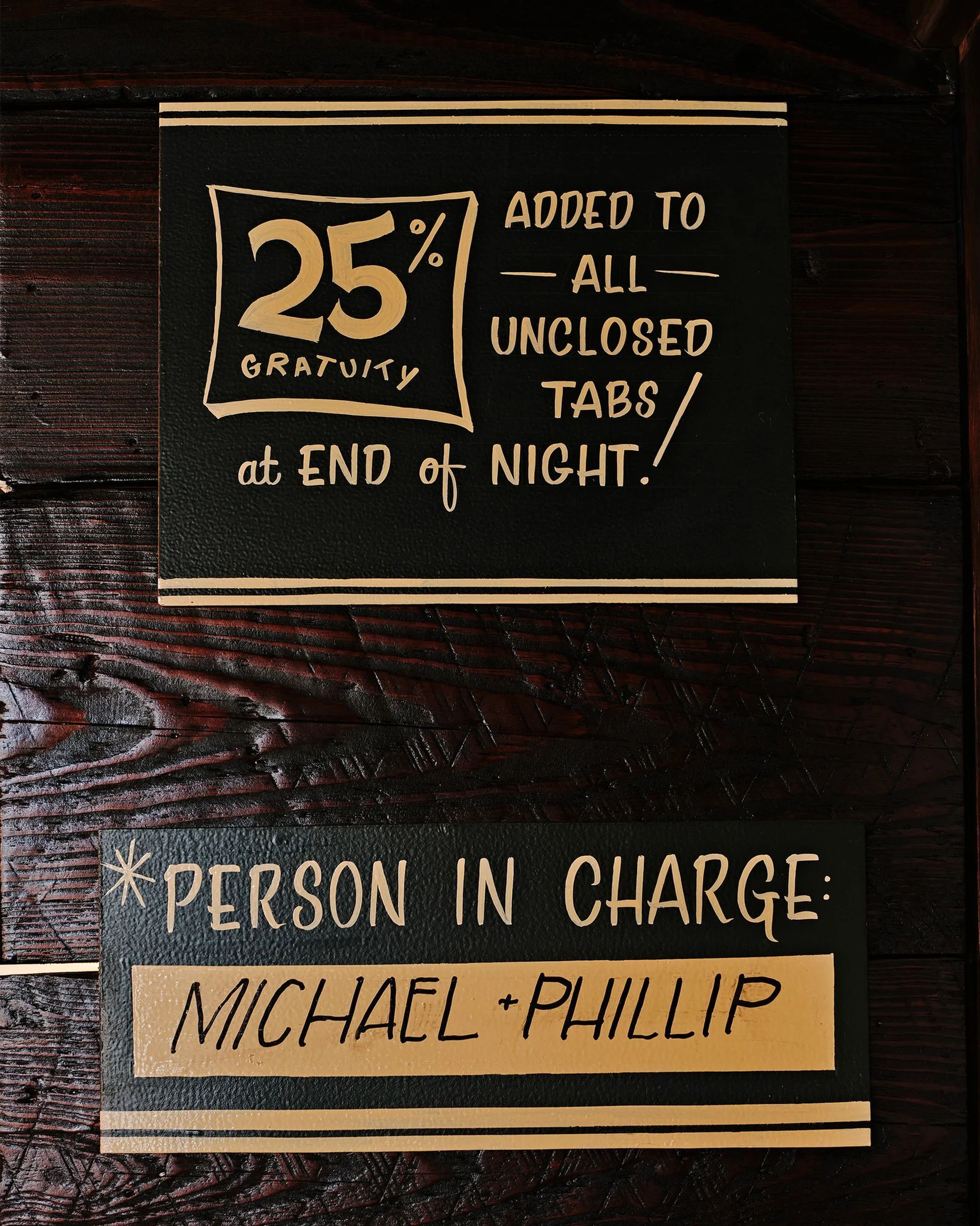 Black and gold typographic signage mounted on a dark wooden textured wall surface for Brand Identity