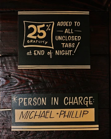 Black and gold typographic signage mounted on a dark wooden textured wall surface for Brand Identity