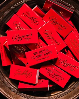Overhead view of bright red matchboxes featuring debossed branding inside a dark metallic bowl