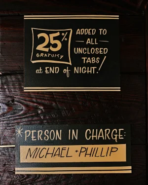 Black and gold typographic signage mounted on a dark wooden textured wall surface for Brand Identity