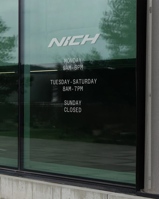 Daytime shot of a building's window displaying business hours for Monday through Sunday, with the business name 'Nich' at the top.