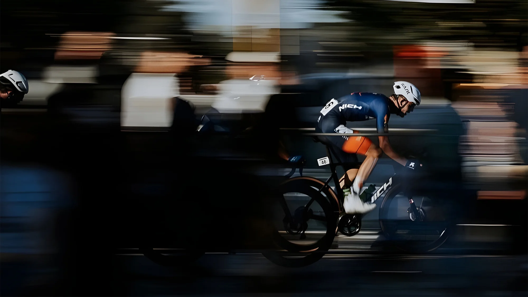 Action shot of a cyclist speeding down a city street, motion blur and crowd in the background. Sports and fast-paced imagery.