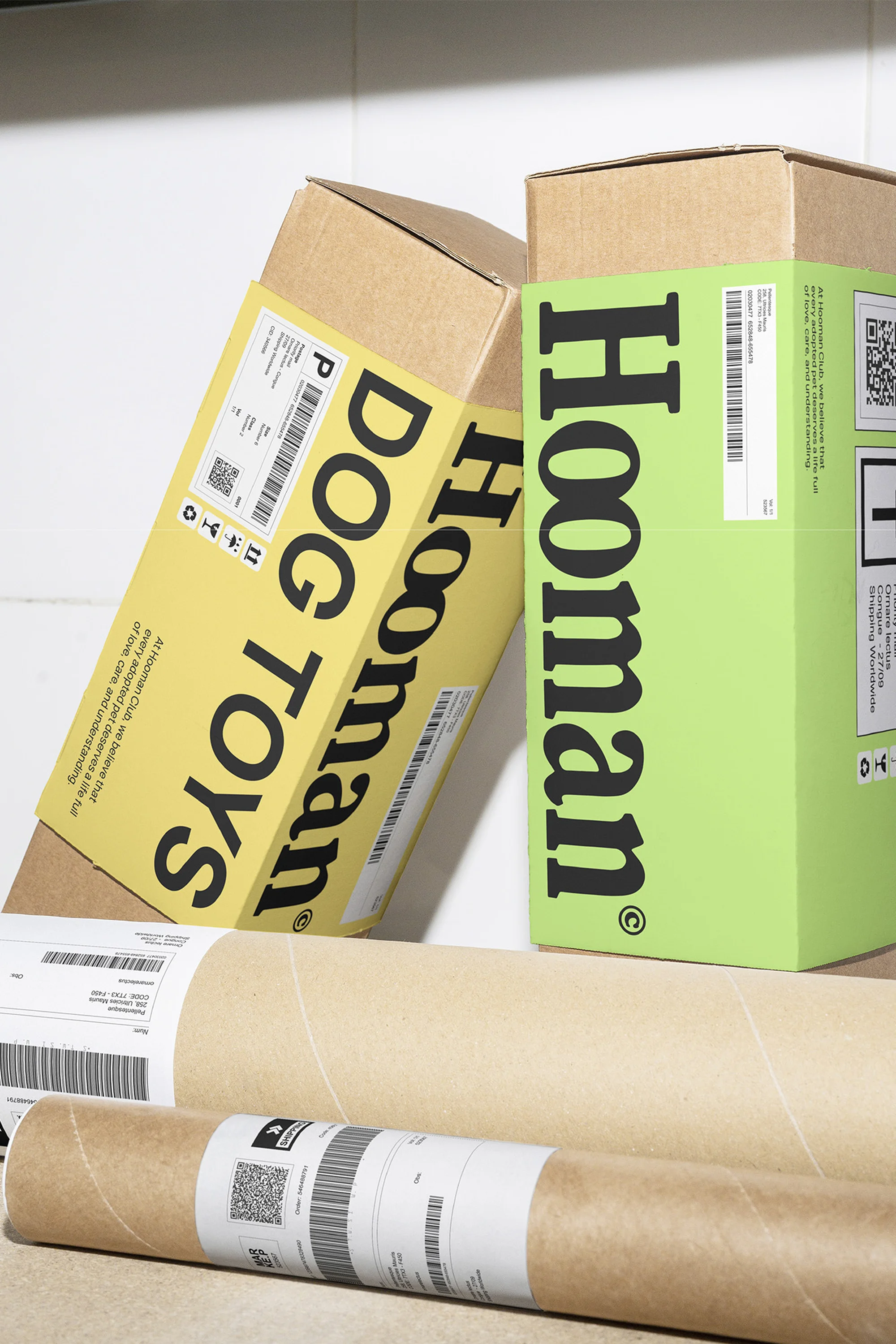 Dog toys subscription boxes from Hooman in yellow and green, arranged on a white shelf with cardboard tubes, in a studio setting.