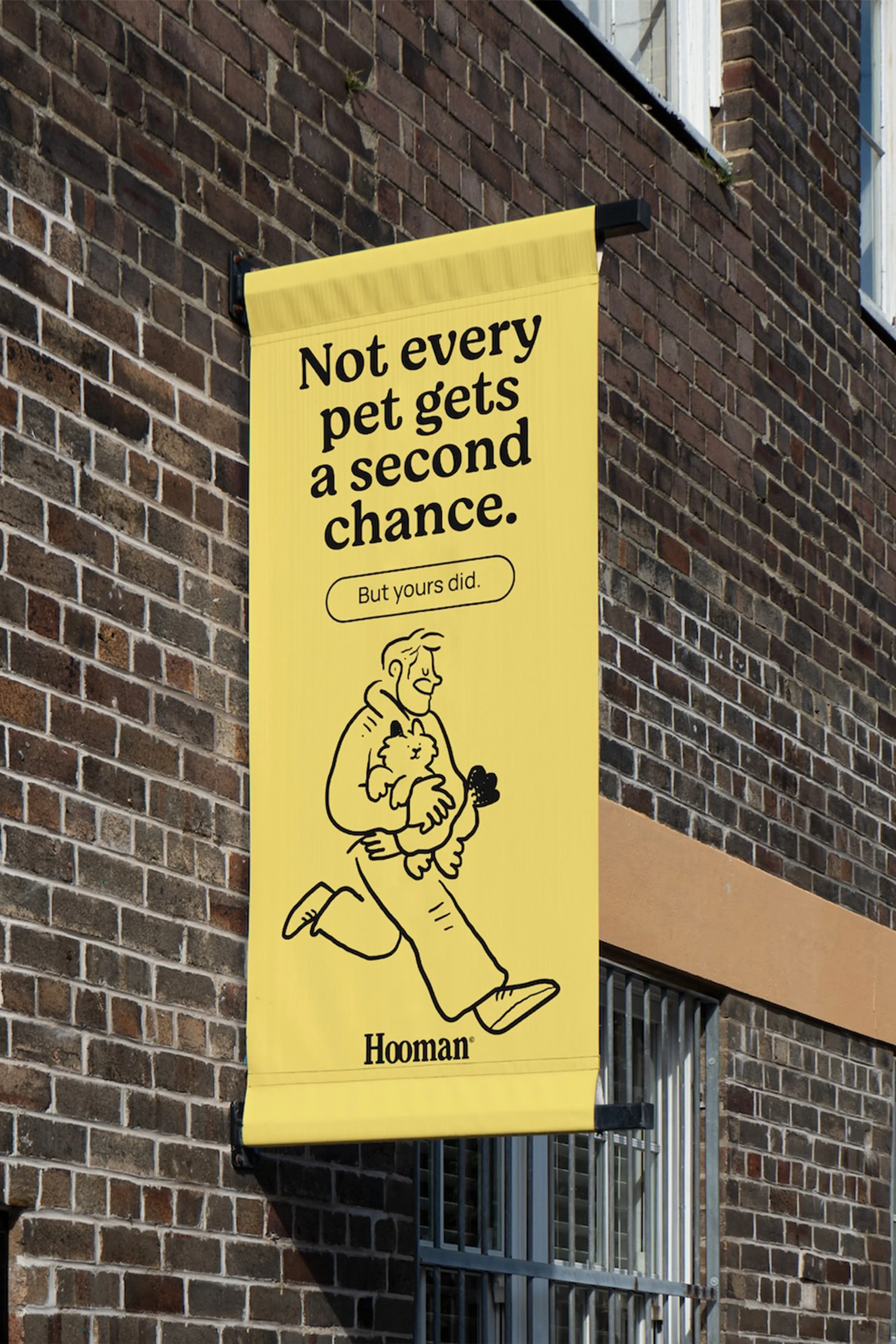 Illustration of a man running while holding a cat, displayed on a yellow vertical banner hanging on a brick building outdoors.