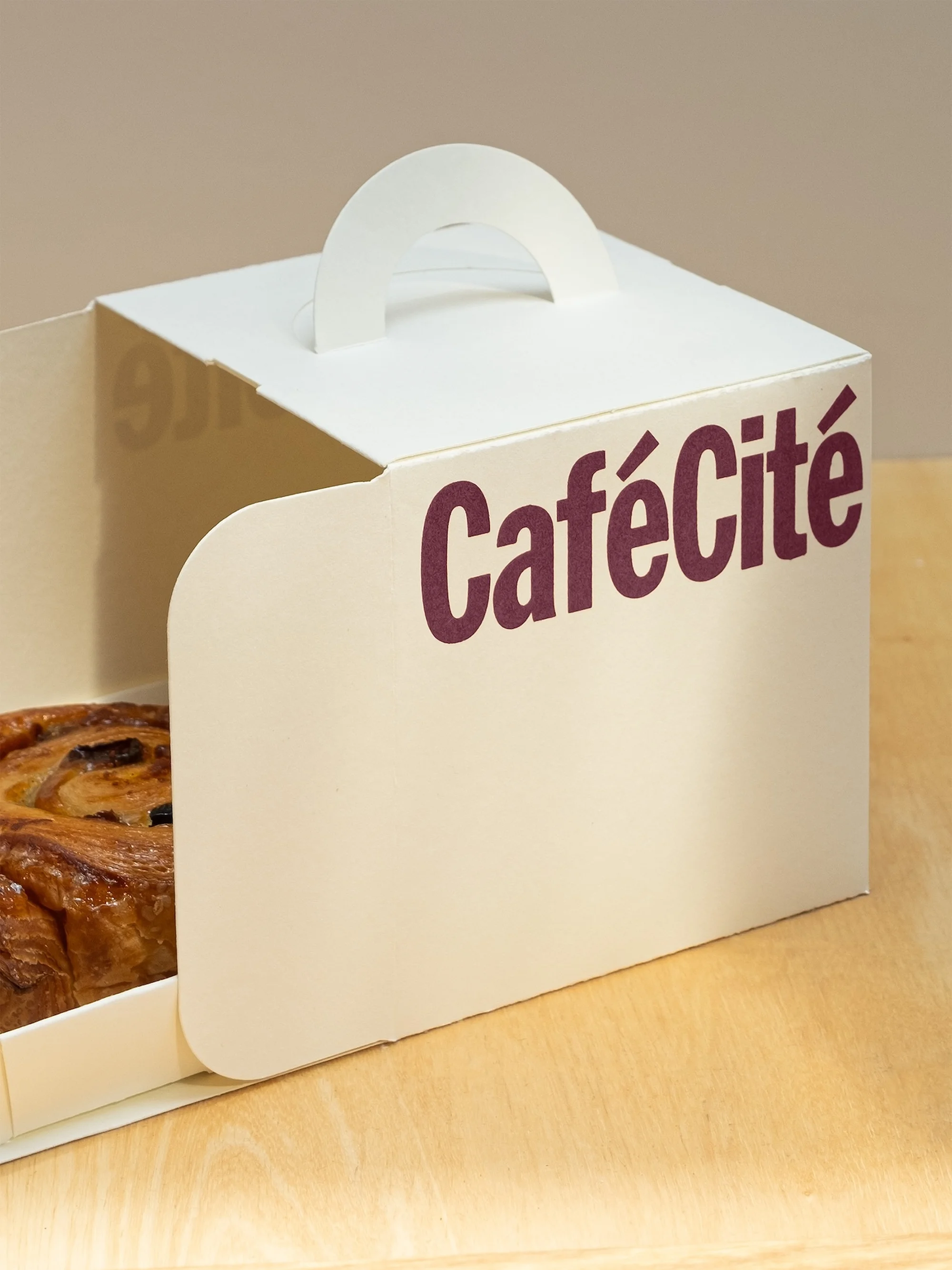 Freshly baked pastry displayed inside a white cardboard box with 'Café Cité' text on the side, set on a light wooden surface.