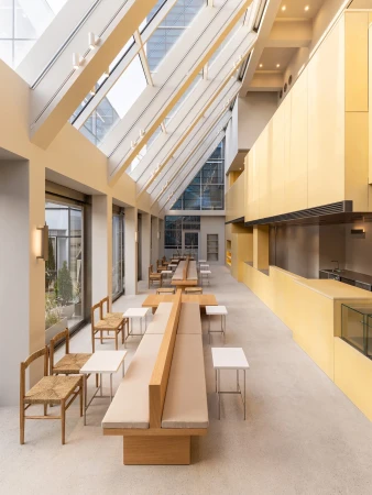 Interior view of a modern café or dining space featuring light wood furniture, a long booth, and a high, angled skylight.