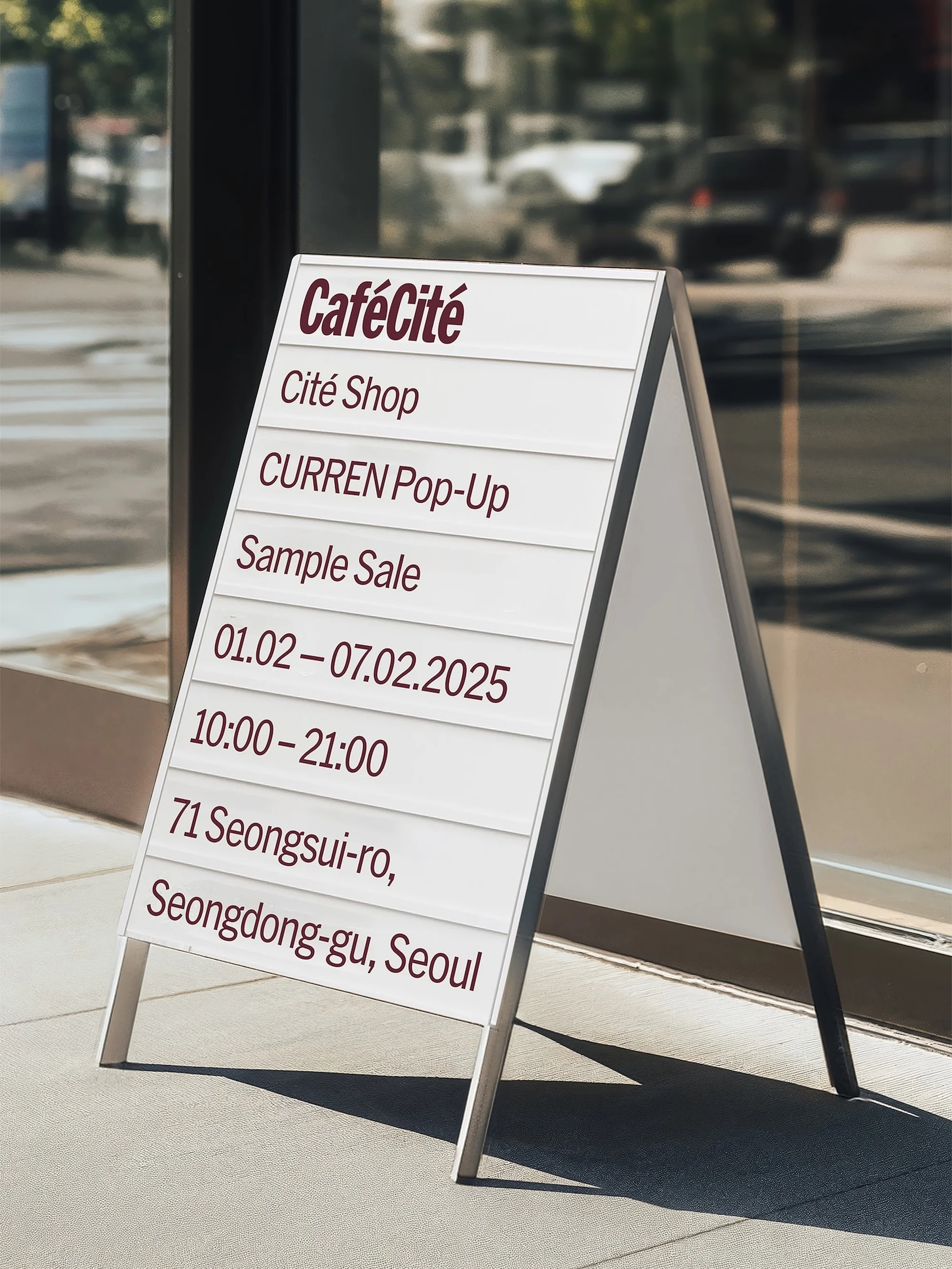A-frame sign in front of a glass storefront. The sign advertises CaféCité, Cité Shop, and a CURREN Pop-Up store in Seoul.