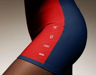 Close-up of an athlete wearing red and blue athletic shorts with white graphic details for the USRowing brand identity.