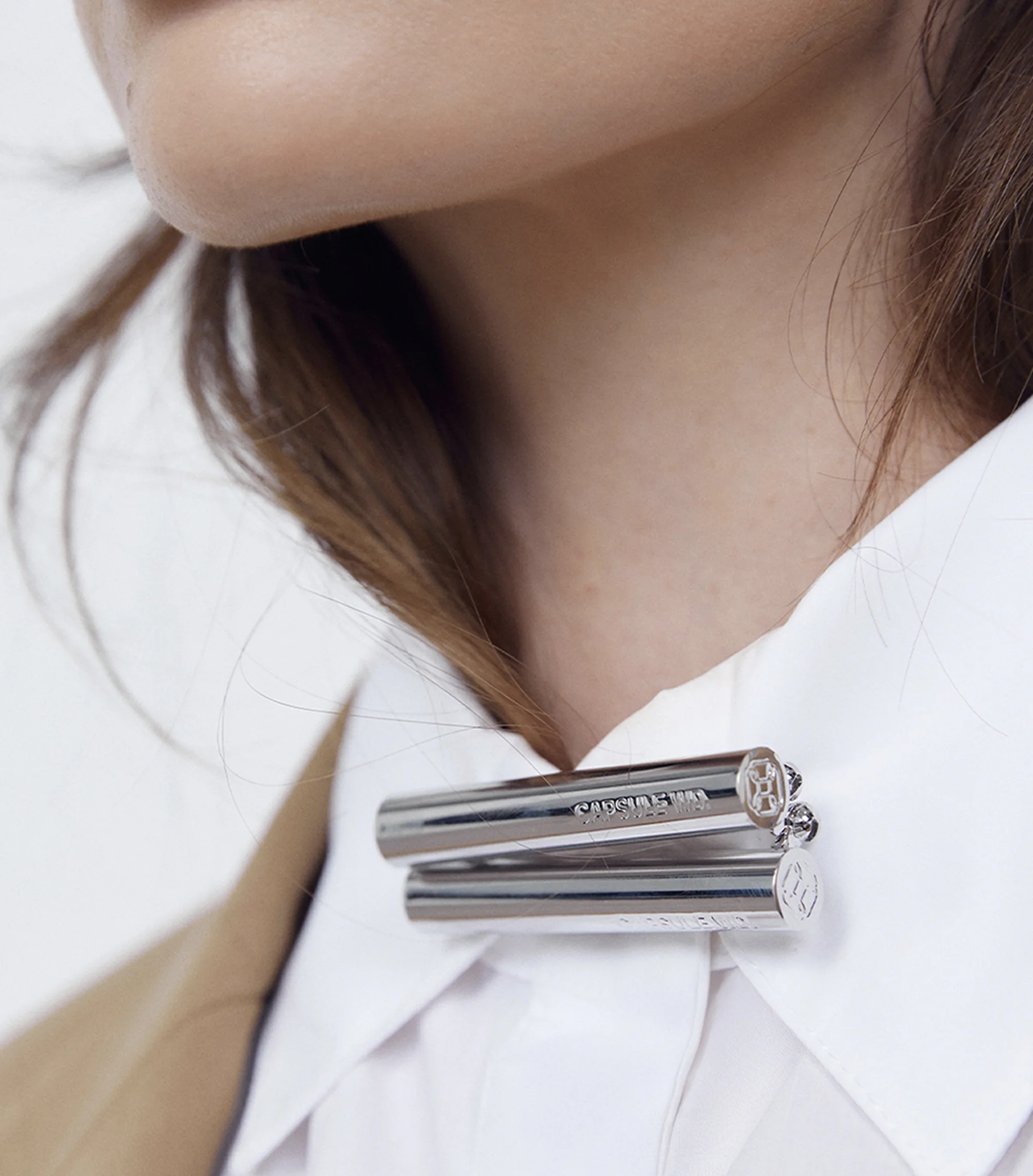 Close-up shot of a woman wearing a white collared shirt with a silver brooch pinned to it, accessorizing with a tan jacket.