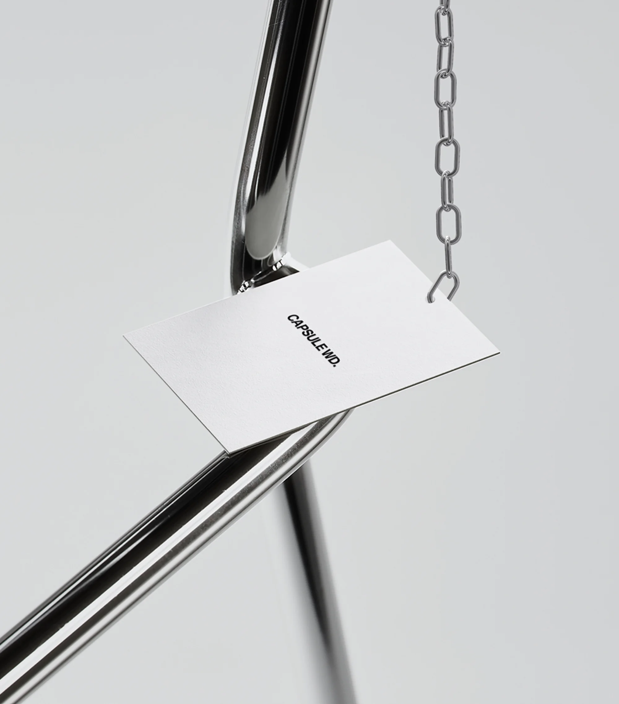 Studio shot of a chrome clothing rack with a white tag hanging from a chain, featuring minimal design and bright, neutral lighting.