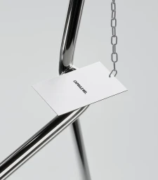 Close-up of a branded metal card hanging from a silver chain against a clean white background for Capsule WD