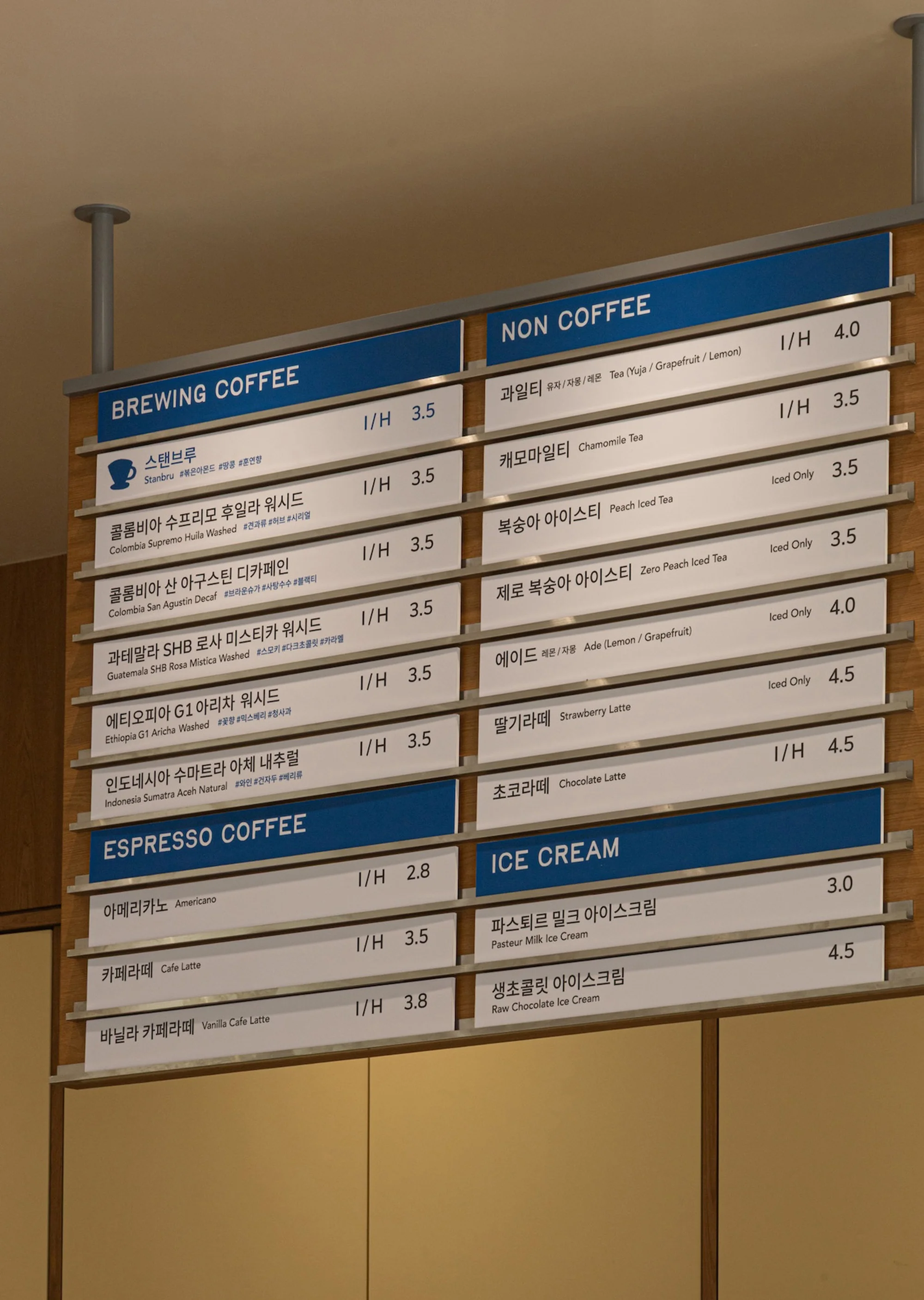 Cafe menu board listing brewing coffee, non-coffee, espresso coffee, and ice cream options with prices in a bright, indoor setting.