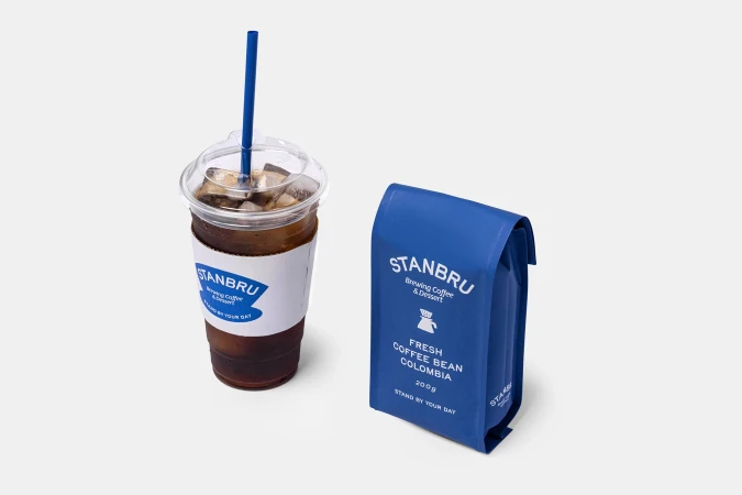 Iced coffee in a clear plastic cup with a blue straw and a blue bag of fresh coffee beans, both featuring the Stanbru logo.