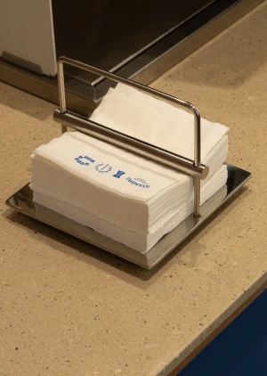 Stainless steel napkin holder filled with white paper napkins on a speckled beige countertop.