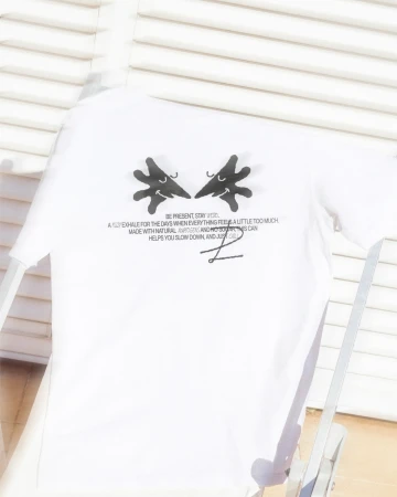 White t-shirt on a chair features playful cartoon hand graphics and text, creating a casual and creative fashion statement.