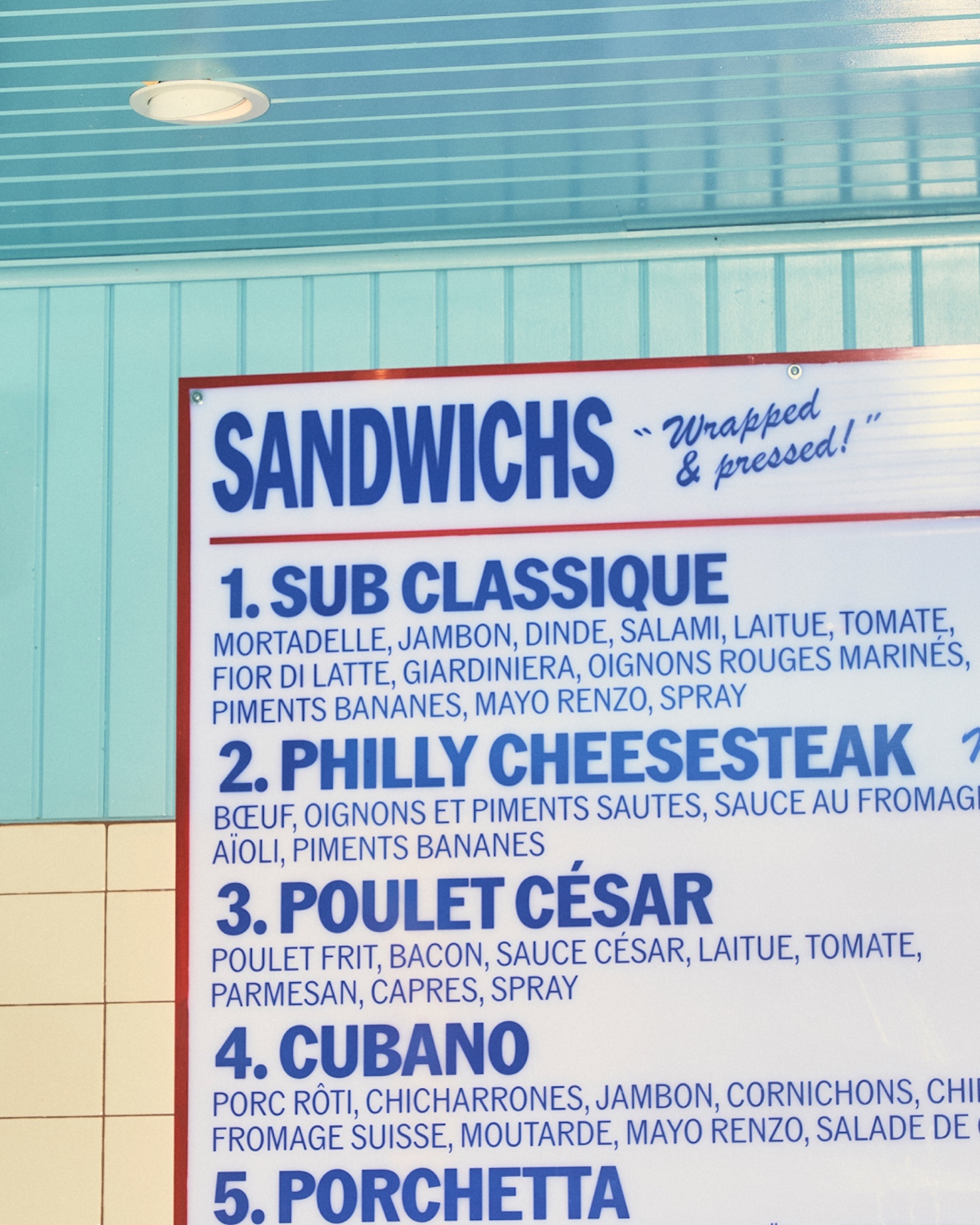 Menu board listing sandwich options with descriptions in a variety of languages, including English, French, and Italian.
