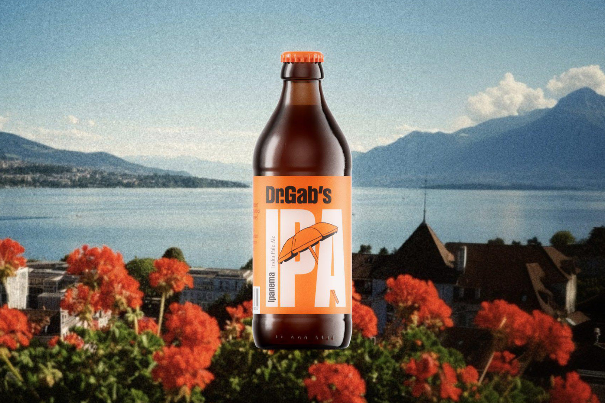 Brown bottle of Dr. Gab's IPA beer with orange label, placed in front of a lake, mountains and red geraniums.