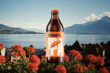 Brown glass beer bottle with orange cap and label positioned in front of a scenic lake view with red flowers.