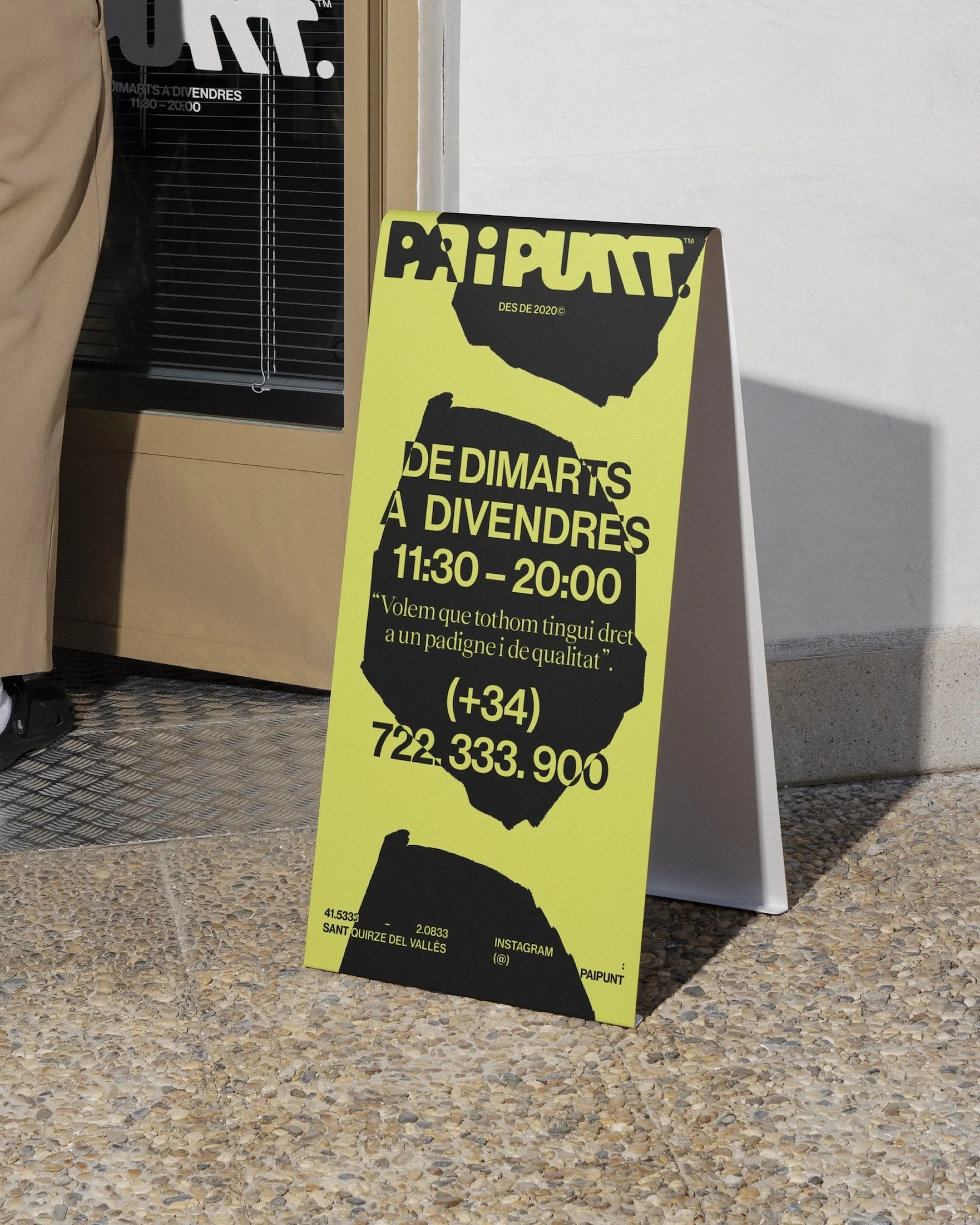 Sidewalk sign with black text on a yellow background, listing hours and contact information for the business, on a city street.