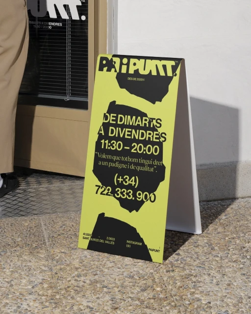 Sidewalk sign with black text on a yellow background, listing hours and contact information for the business, on a city street.