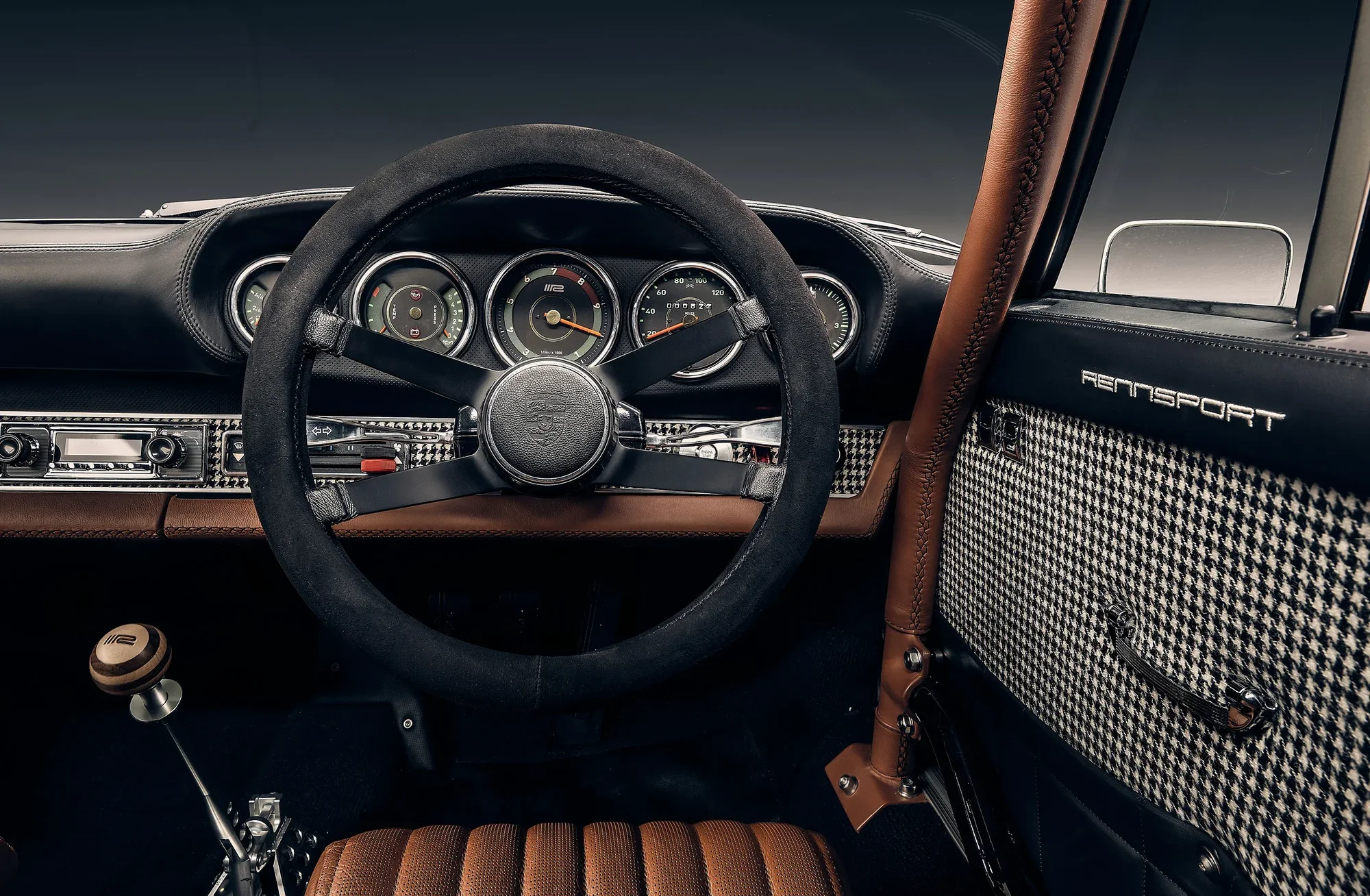 Interior view of a classic Porsche featuring a black steering wheel, dashboard gauges, and houndstooth patterned door panel.