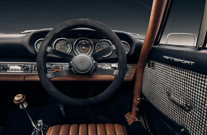 Interior view of a classic Porsche featuring a black steering wheel, dashboard gauges, and houndstooth patterned door panel.