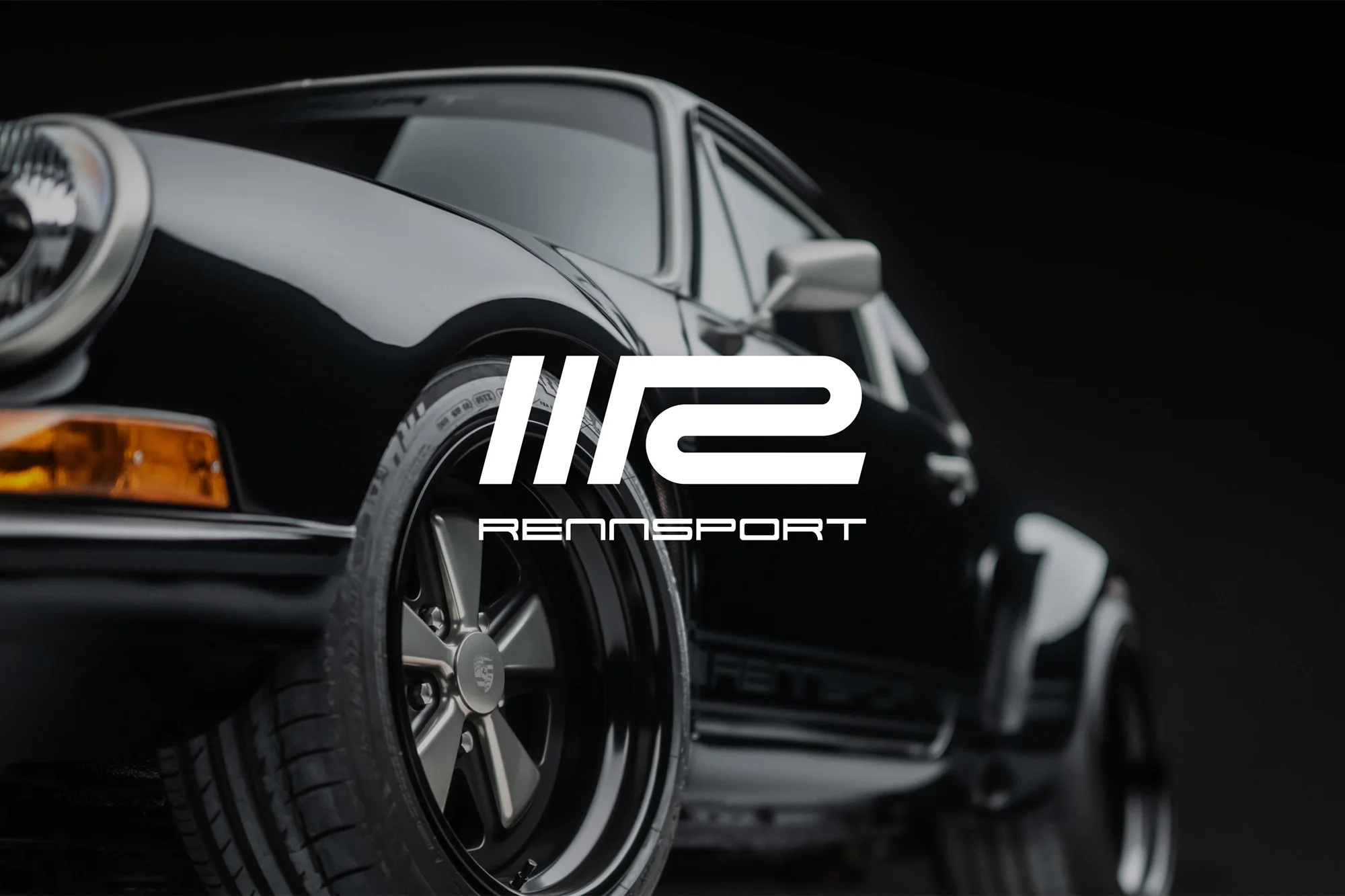 A black vintage Porsche 911 is showcased with the Rennsport logo prominently displayed against a sleek black background in a studio shot.