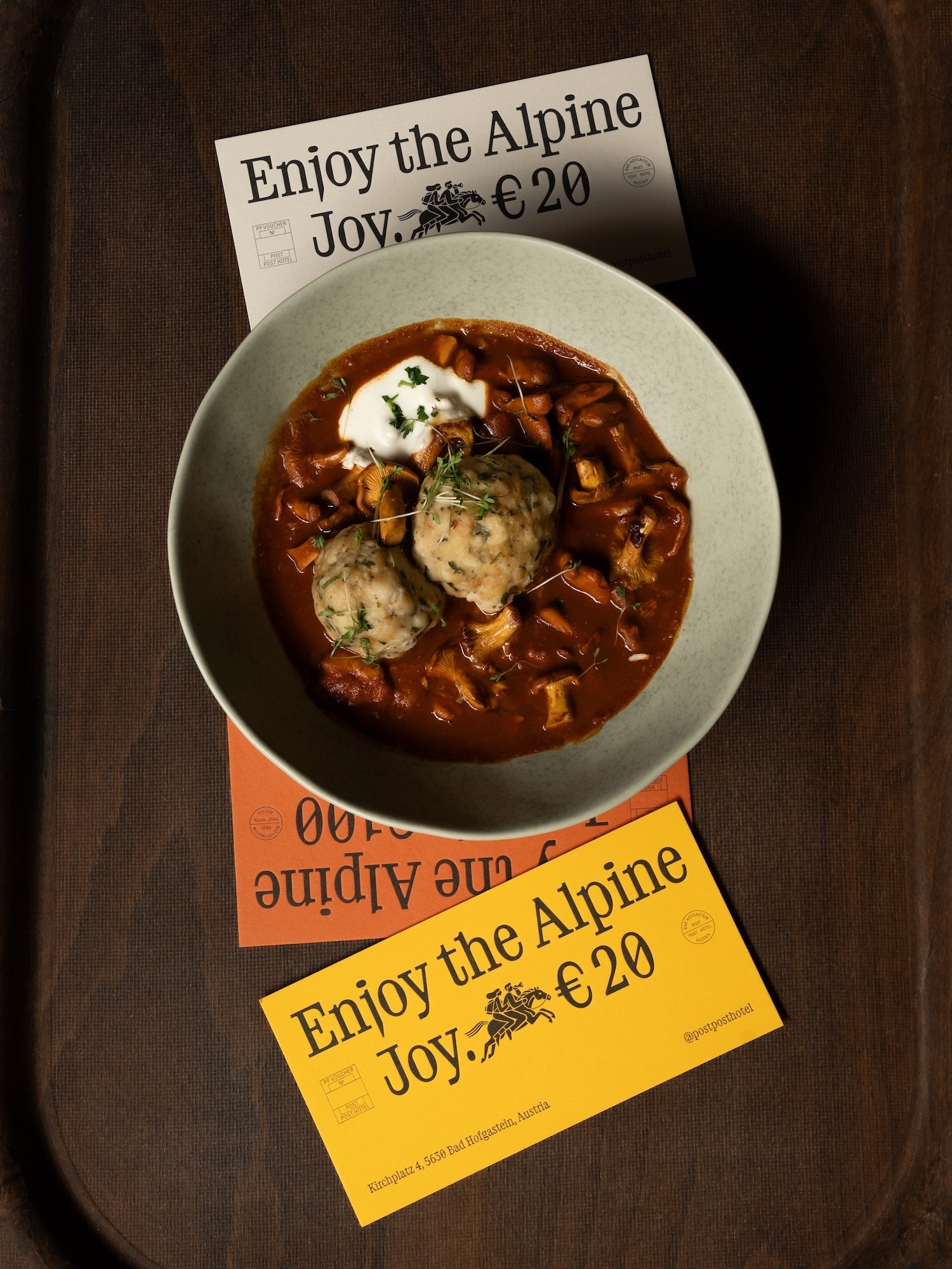Overhead shot of creamy mushroom stew with dumplings in a light green bowl, set on a dark wooden surface with promotional cards.