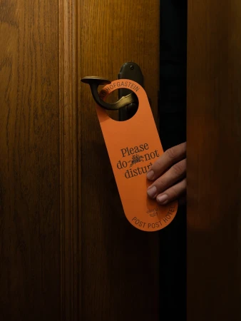 Hand placing 'Do Not Disturb' sign on a dark wood hotel room door handle, illuminated by warm light, creating an inviting atmosphere.