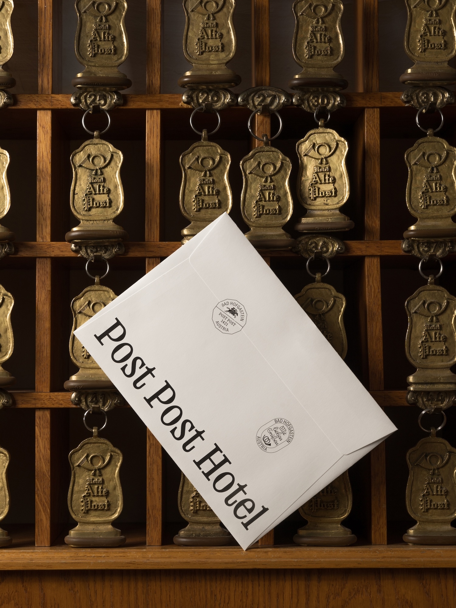 An envelope rests against vintage hotel key tags in a wooden rack, suggesting travel, hospitality, and timeless correspondence.