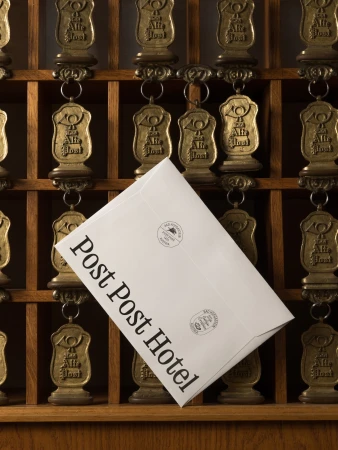 An envelope rests against vintage hotel key tags in a wooden rack, suggesting travel, hospitality, and timeless correspondence.