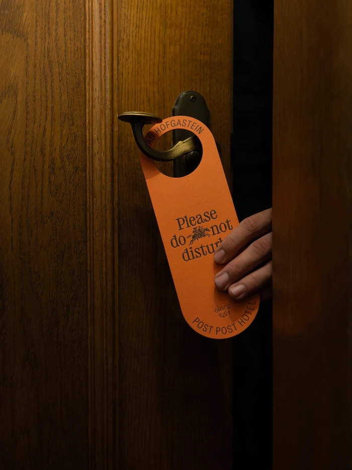 Orange doorknob hanger hanging on a dark wood door handle with a hand touching it