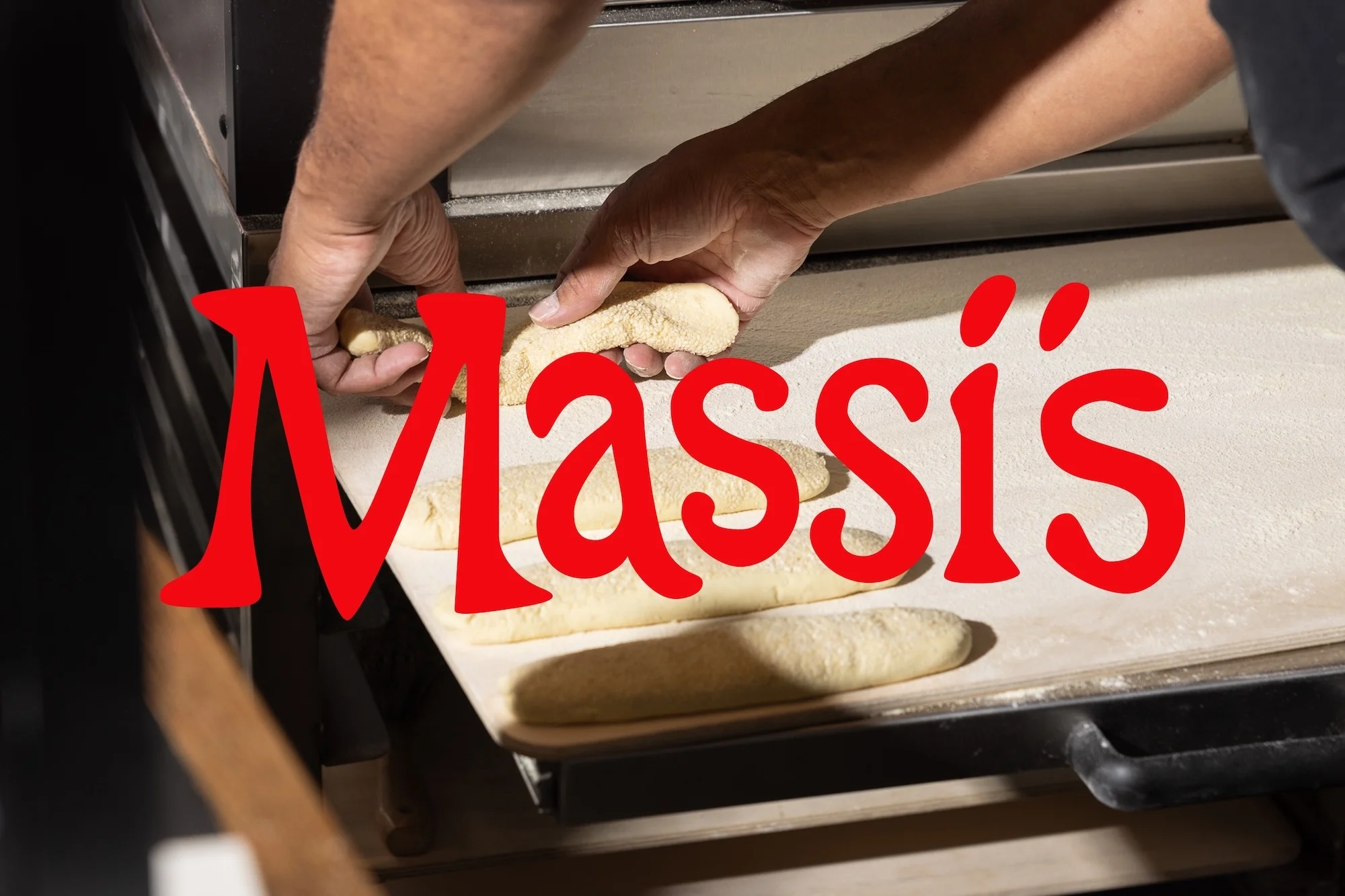 A baker places dough on a baking sheet next to an oven, preparing to bake fresh bread in a commercial kitchen, bright indoor lighting.
