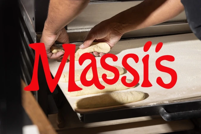 A baker places dough on a baking sheet next to an oven, preparing to bake fresh bread in a commercial kitchen, bright indoor lighting.