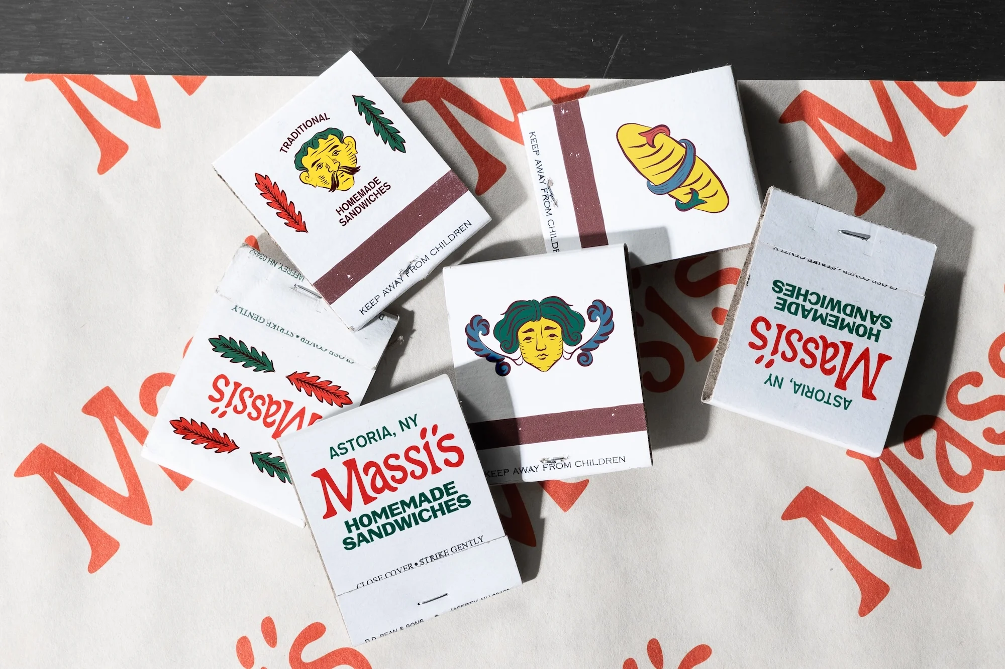 Several matchboxes with retro designs, showcasing illustrations and text related to homemade sandwiches, are arranged on a patterned surface.