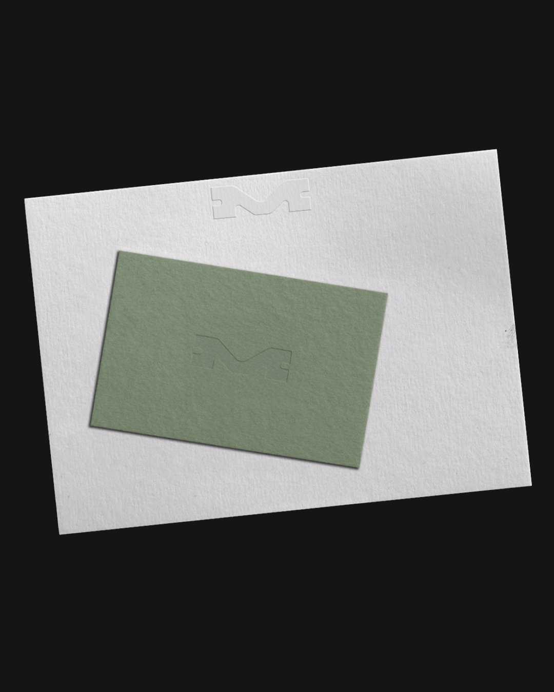 Close-up of a light green business card placed on top of a white paper with embossed logo, set against a solid black background.