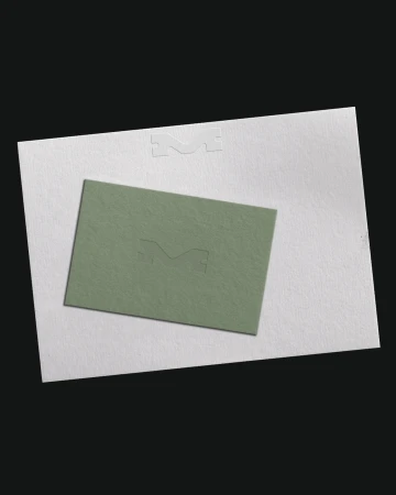 Close-up of a light green business card placed on top of a white paper with embossed logo, set against a solid black background.