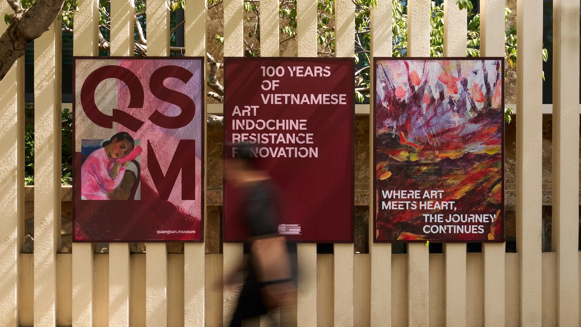 Three art posters on a wall advertise the Quàng San Museum with colorful art, text, and figure, displayed outdoors.