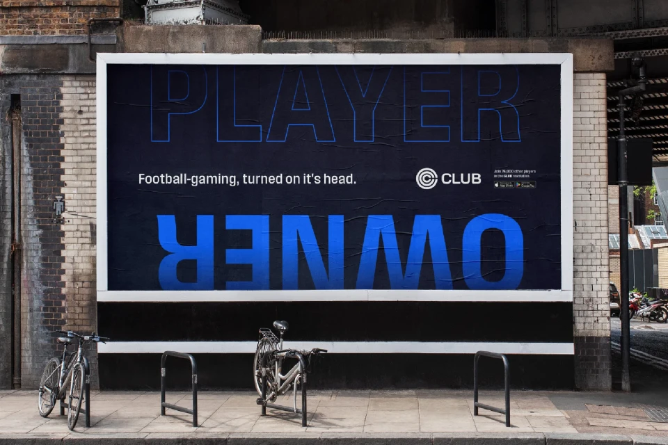 Billboard advertisement for a football gaming app with bicycles parked nearby in an urban setting. Bold blue and white text on a dark background.