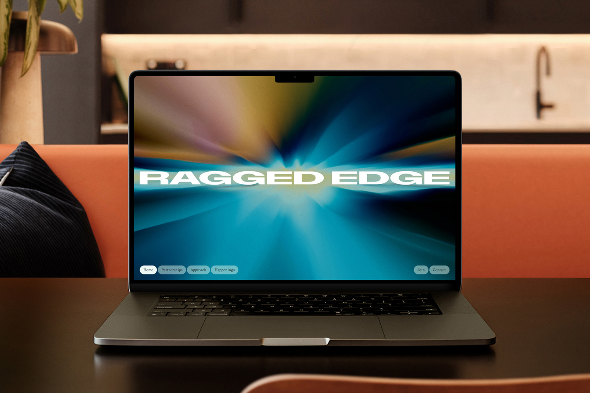 Laptop displaying graphic design with blurred background, set on a table in a modern interior with an orange couch and minimalist design.