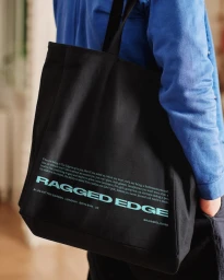 Person wearing a blue shirt carries a black canvas tote bag printed with teal branding text.