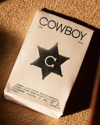White paper packaging for Cowboy coffee featuring bold black typography and a sheriff badge graphic on burlap fabric.