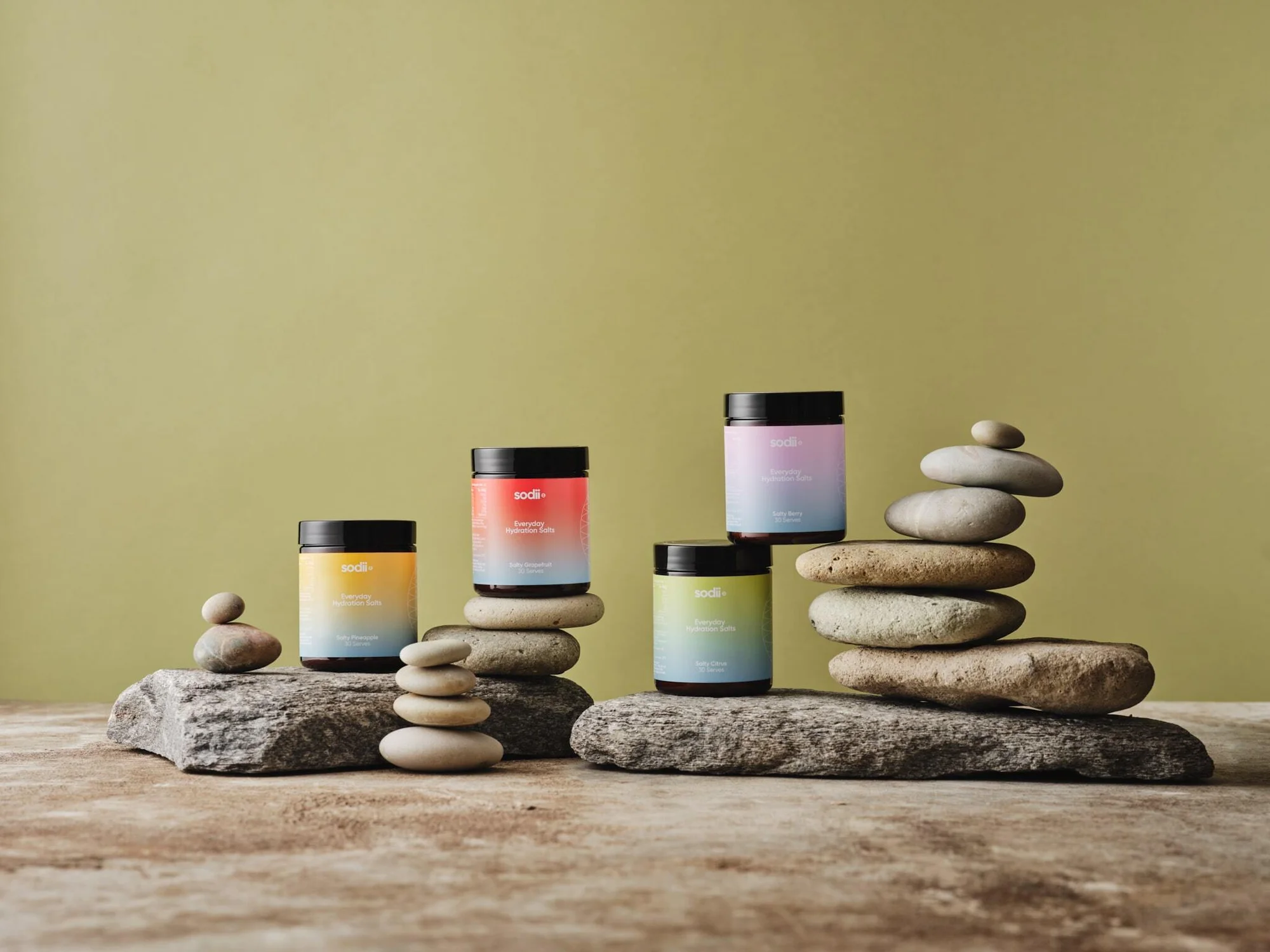 Elevated view of skincare product jars from Sodi arranged on rough stones and stacked pebbles against a muted green background.