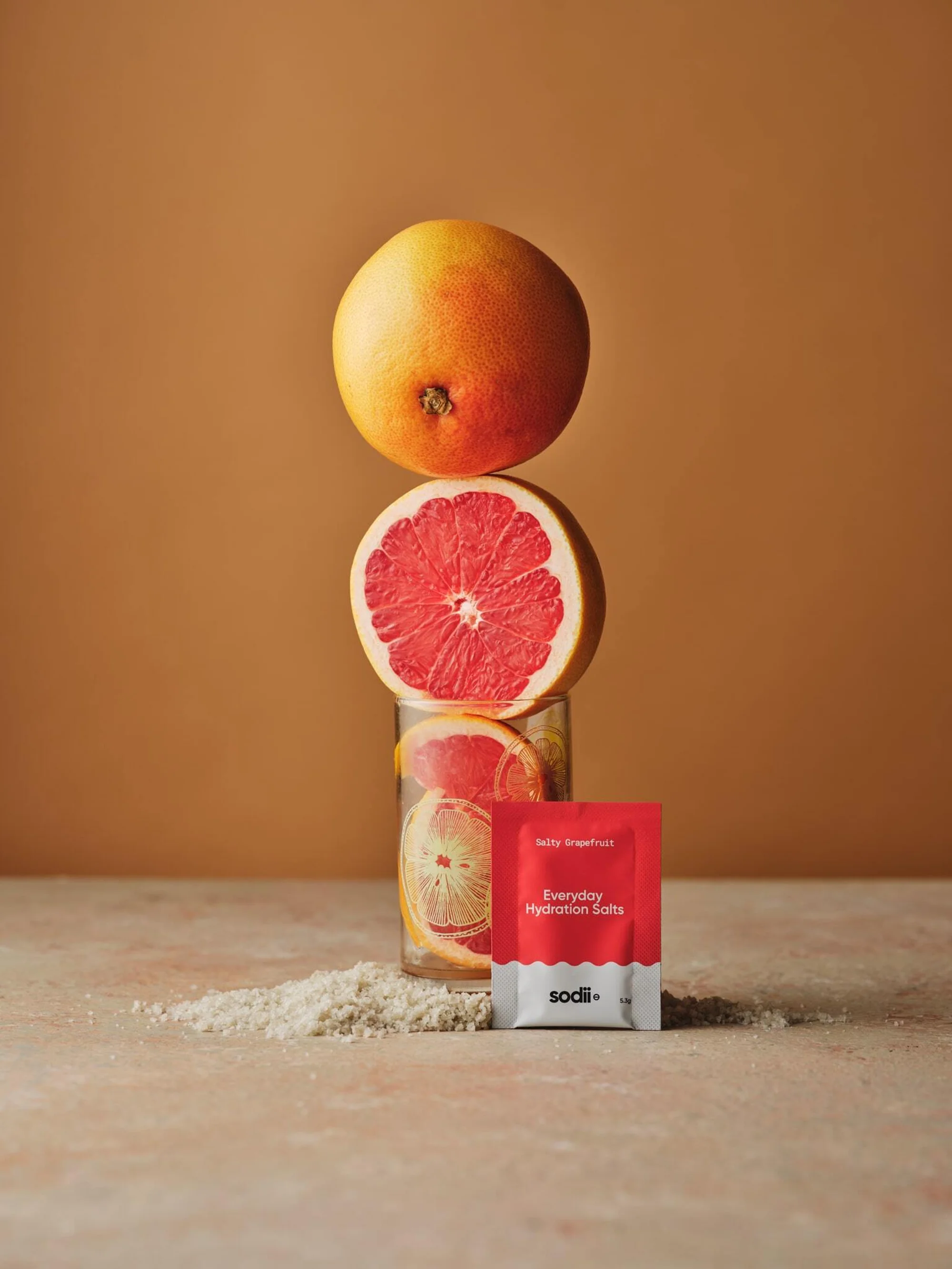 Stack of grapefruit with packaging on peach surface against brown background. Fresh citrus fruit arranged in a minimalist style.