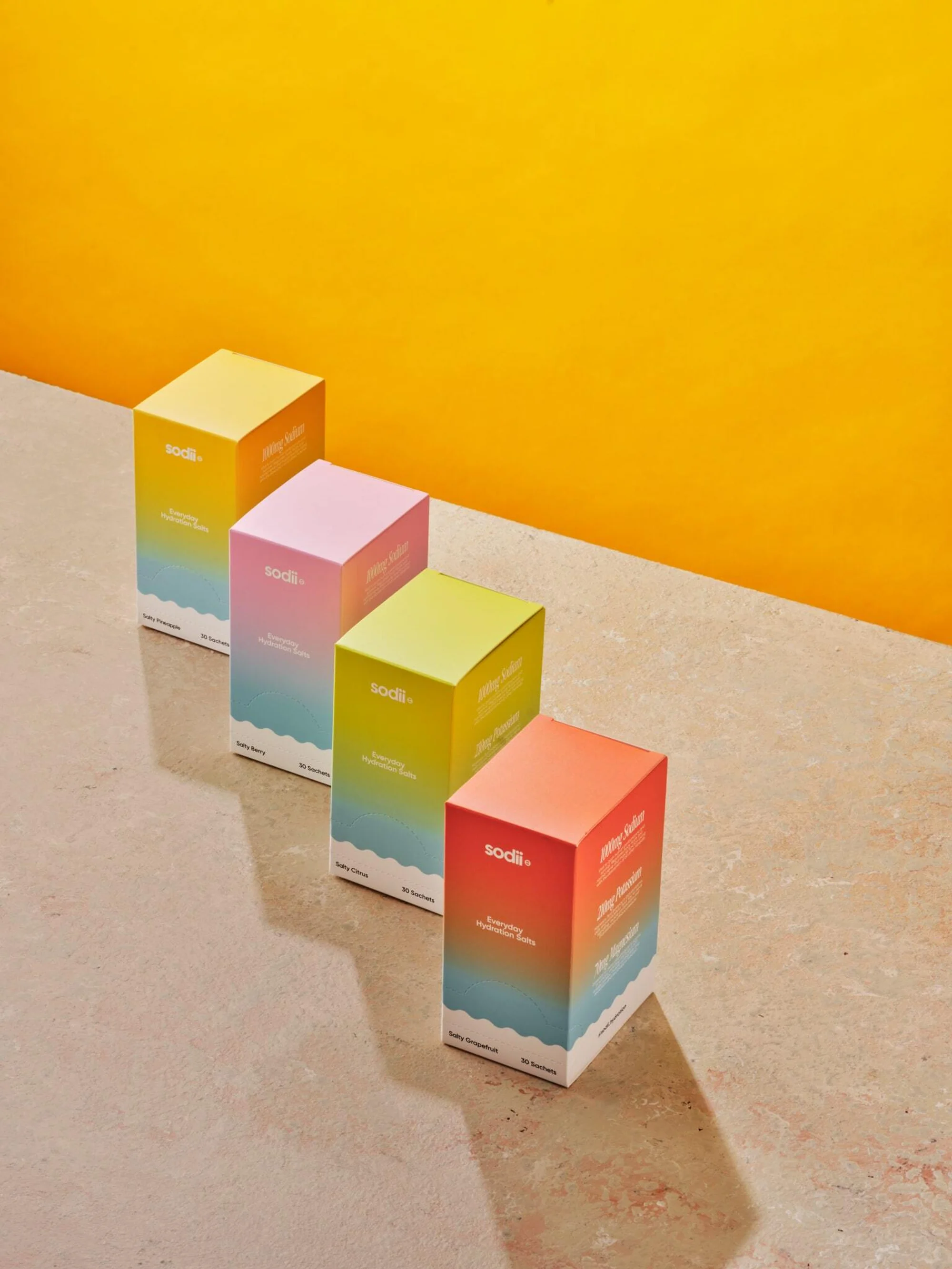 Four colorful Sodi boxes in a row against a gradient background, studio shot with bright lighting and shadows, product photography.