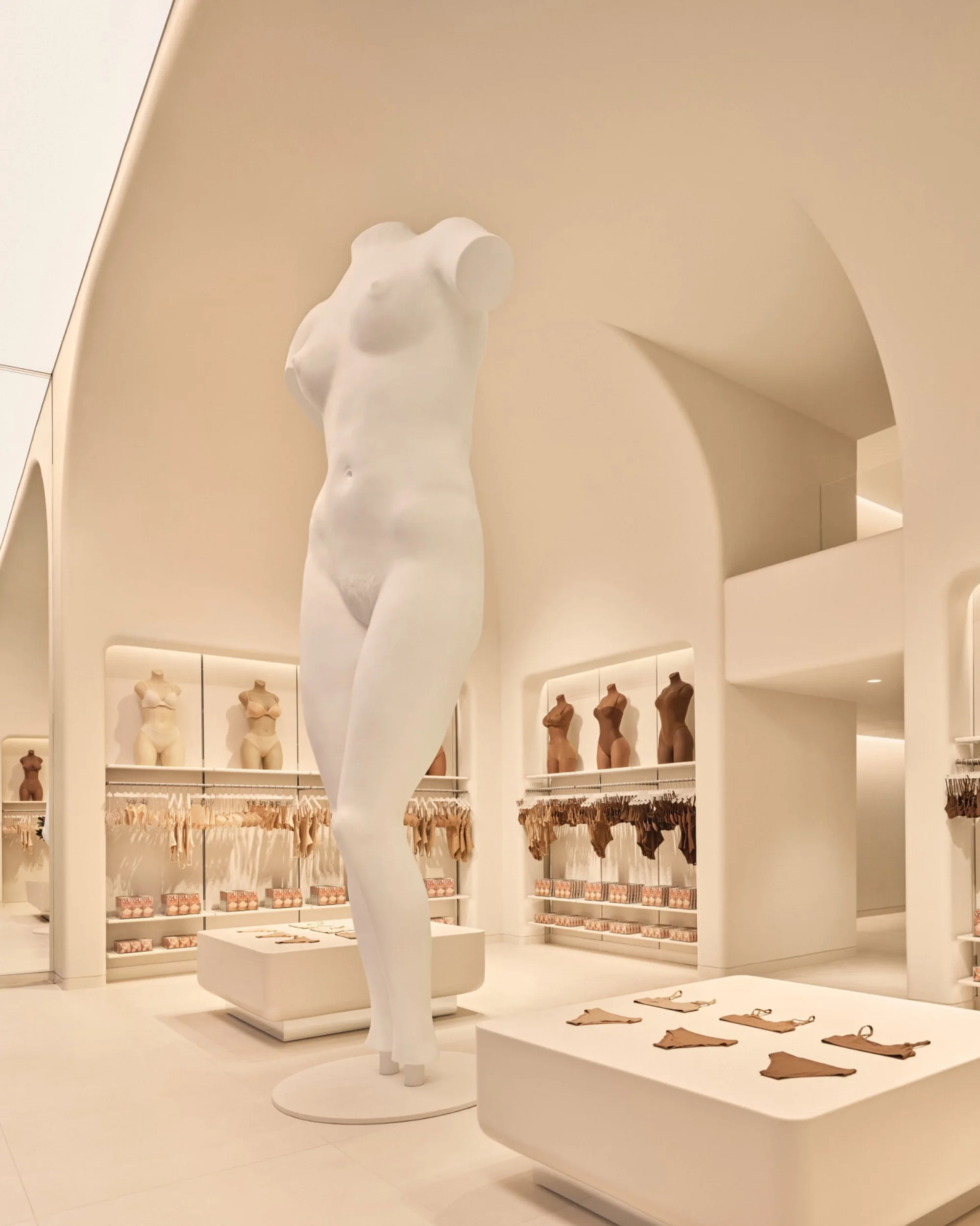 Brightly lit retail space features a white mannequin, displays of neutral lingerie, and clean modern architectural details.