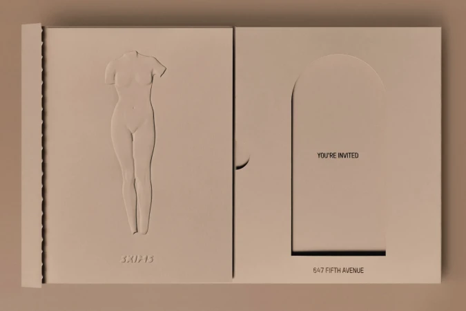Invitation card with a nude female body bas-relief and a minimalist archway design, presented in a light beige color palette.