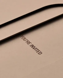 Close-up of a beige envelope featuring the embossed text YOU ARE INVITED on heavy textured paper.