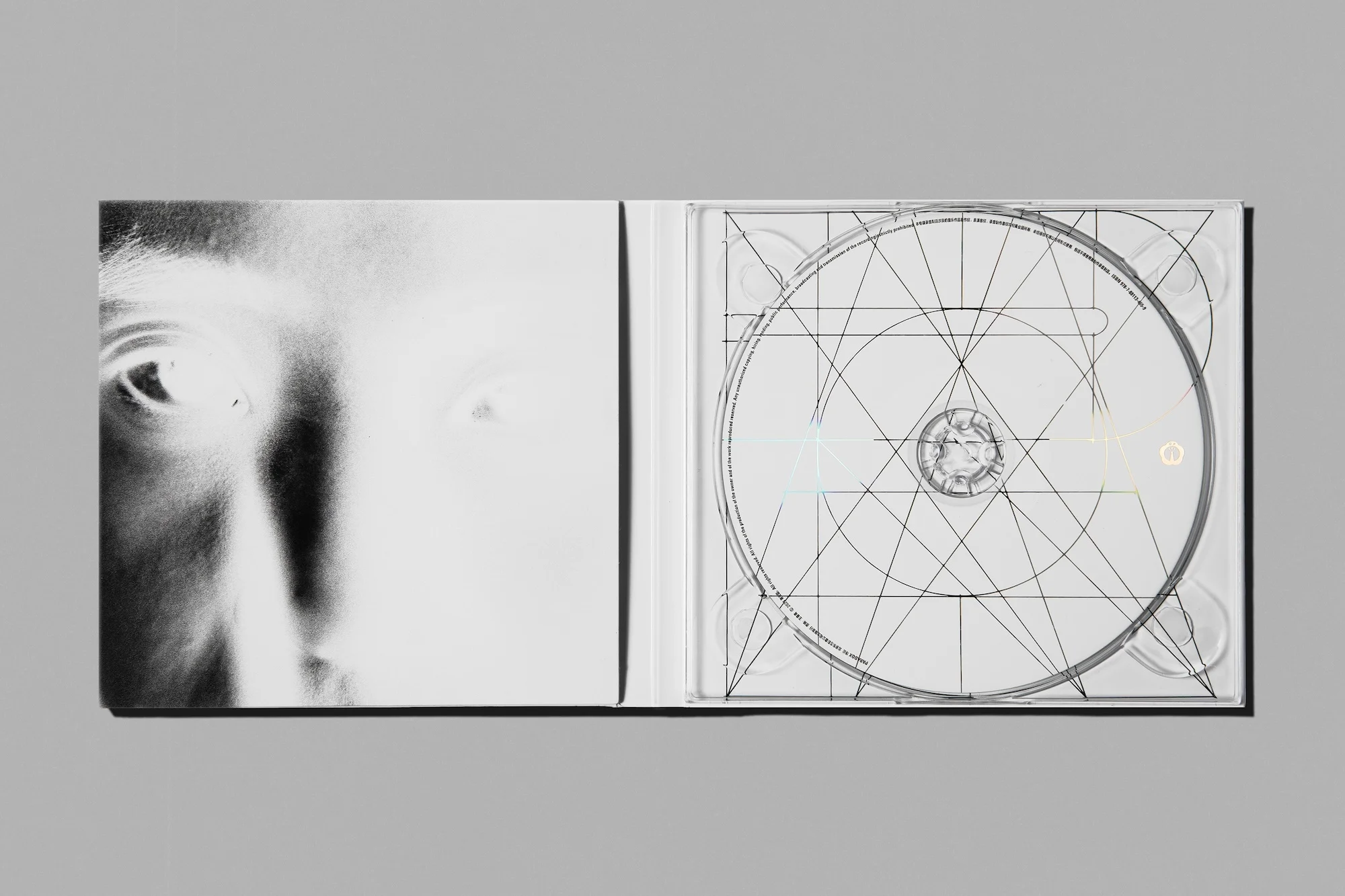 Monochromatic image of an opened CD case featuring a partial face on the left and a CD with geometric designs on the right.